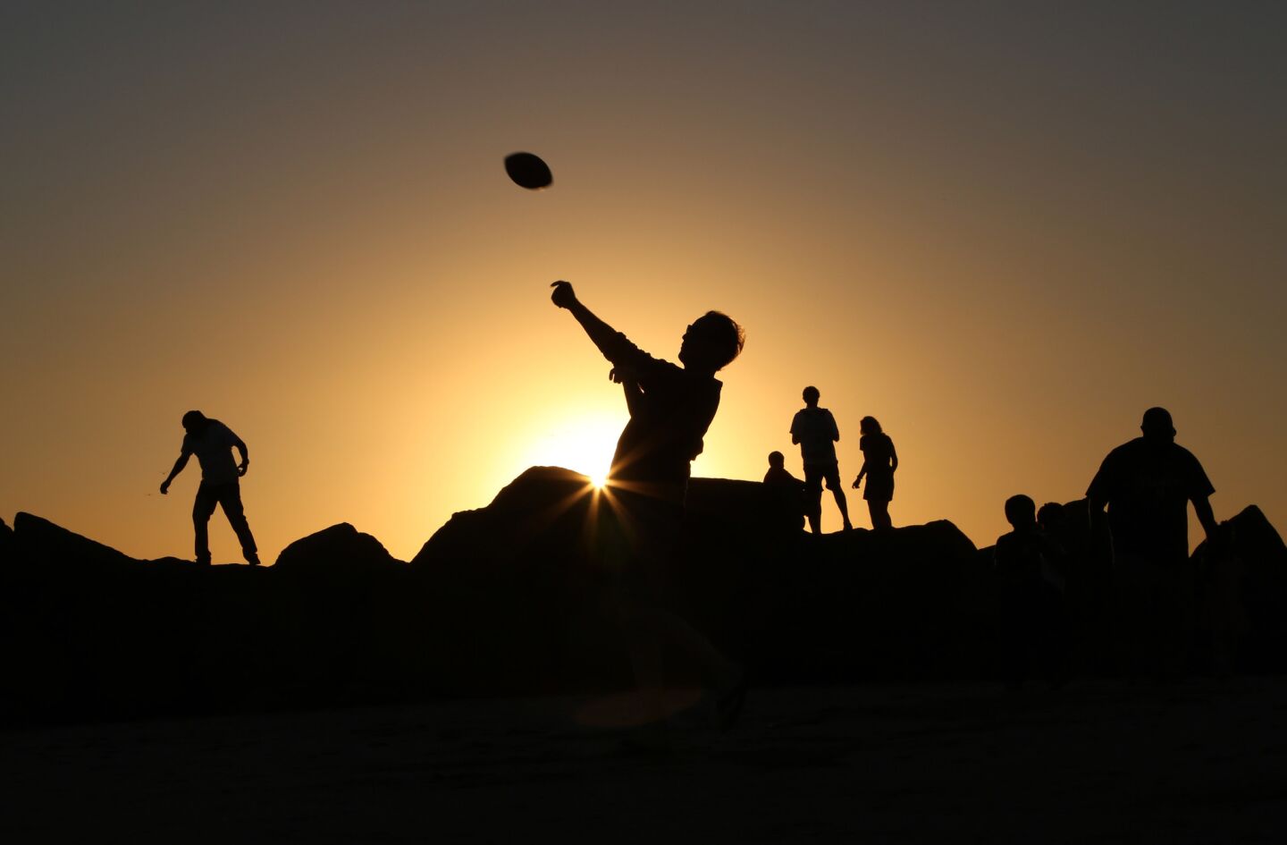 People play football and climb on the rock jetty at Venice Beach.