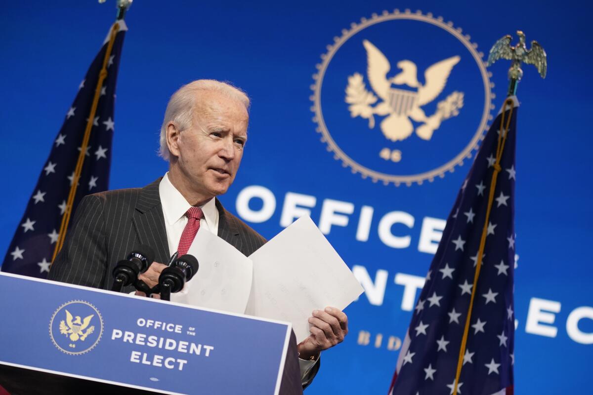 Joe Biden holds papers while speaking at a lectern labeled Office of the President Elect