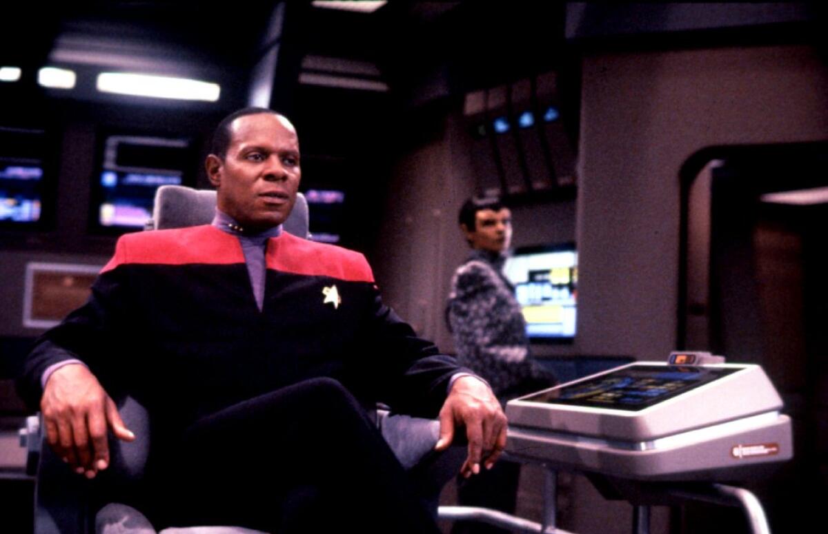 A man in uniform sits in a chair on the deck of a spaceship