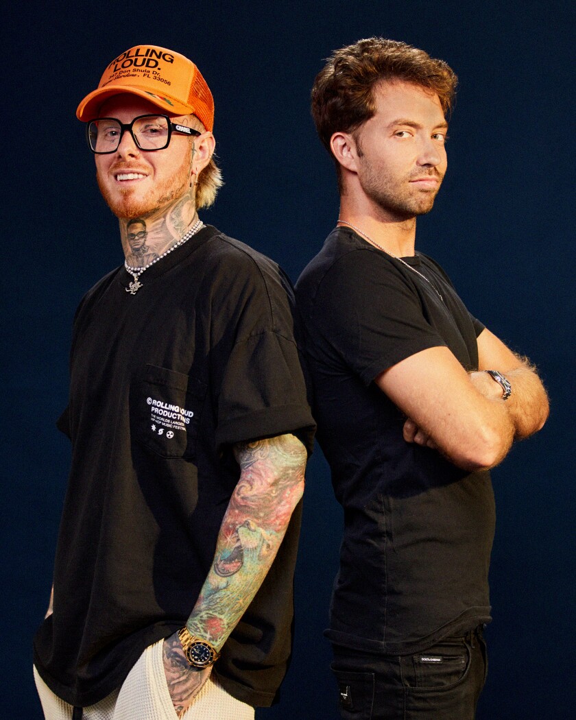 Two young guys in black T-shirts stand back to back.