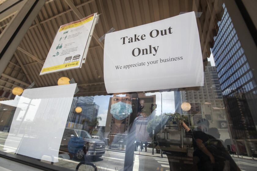 LOS ANGELES, CA - JULY 01, 2020: Charlotte Chacon, Assistant General Manager at The Original Pantry in Downtown Los Angeles, tapes a sign to the window letting customers know that they are now only open for take out service. California Gov. Gavin Newsom announced today that for the next 3 weeks, restaurants in Los Angeles County and a number of other counties statewide will only be allowed to have take out and delivery service due to an increase in coronavirus cases. (Mel Melcon / Los Angeles Times)