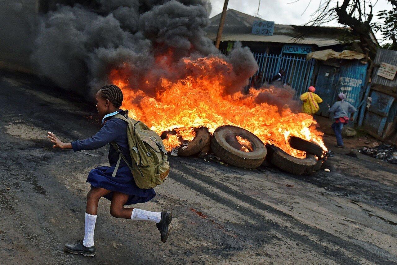 A schoolgirl runs past a burning barricade in Kibera slum, Nairobi, as Kenyan opposition supporters protest for a change of leadership ahead of a vote due next year.