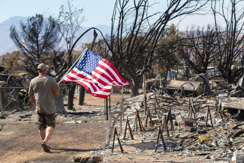 James Hoover of South Lake carries an American flag to post at the corner of his property over the burned-out remains of his home of 17 years, destroyed by the Erskine fire. He hung the flag as a signal of hope to his neighbors.
