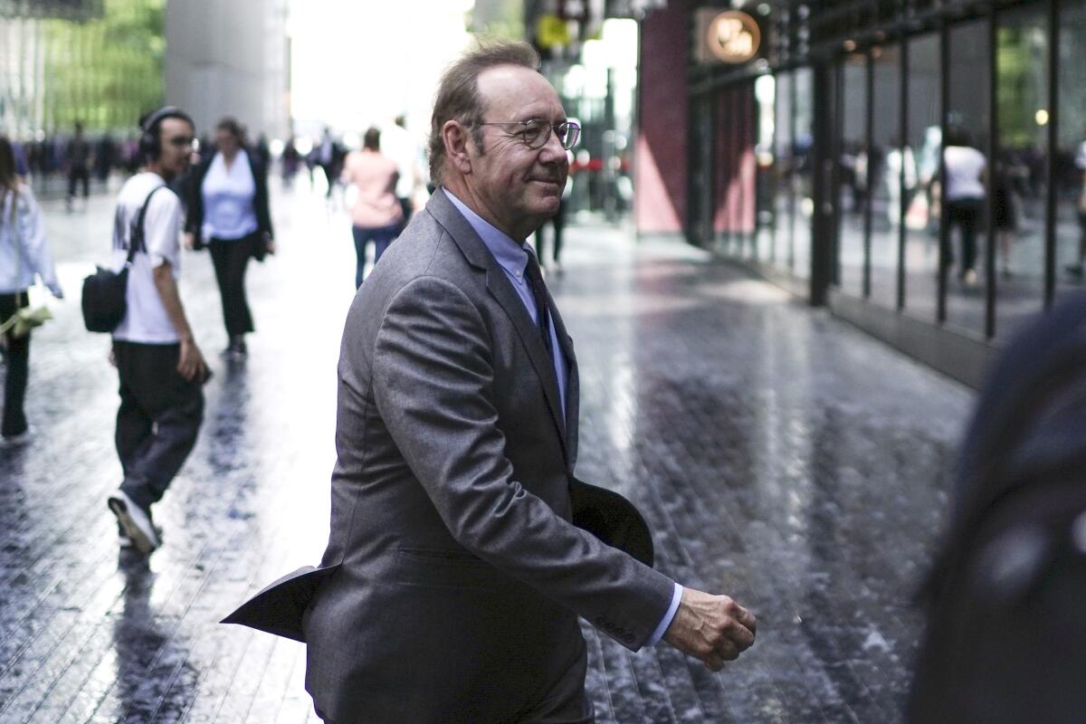 Kevin Spacey, wearing a suit and tie, walks across a London street.