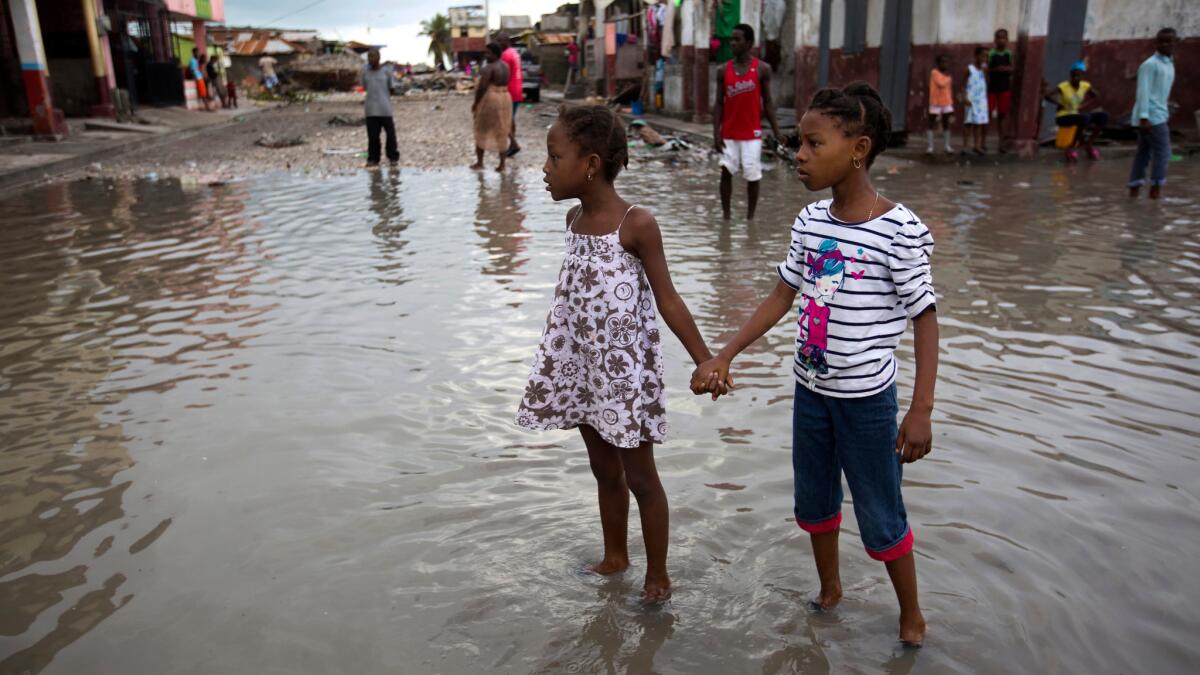 Girls help each other wade through a flooded street after the passing of Hurricane Matthew in Les Cayes, Haiti.