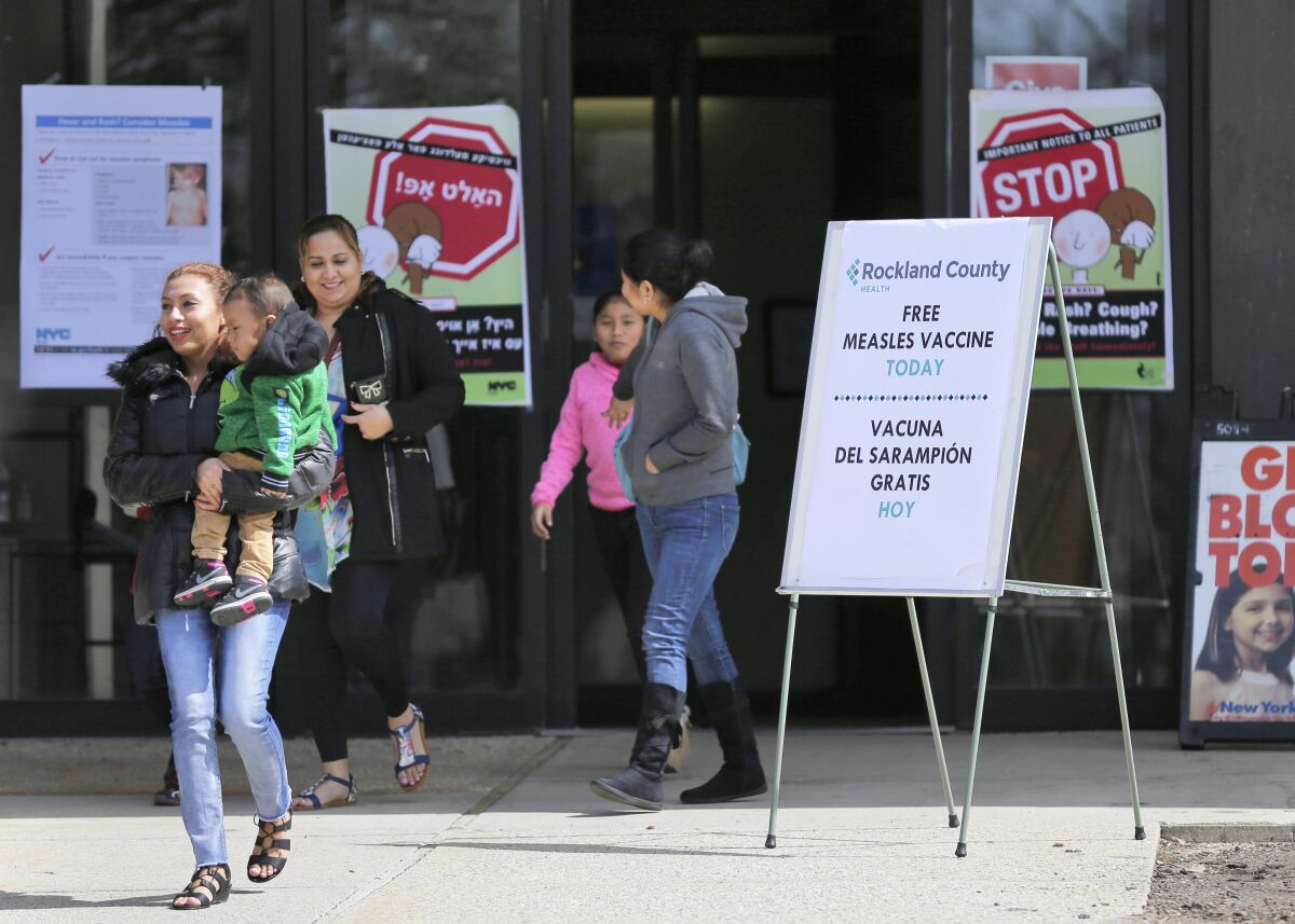 Caretakers and children walk past signs advertising measles vaccines