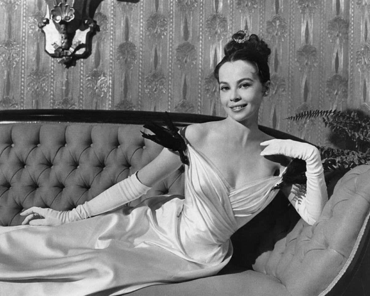 A woman in an evening gown and gloves lies on a couch.