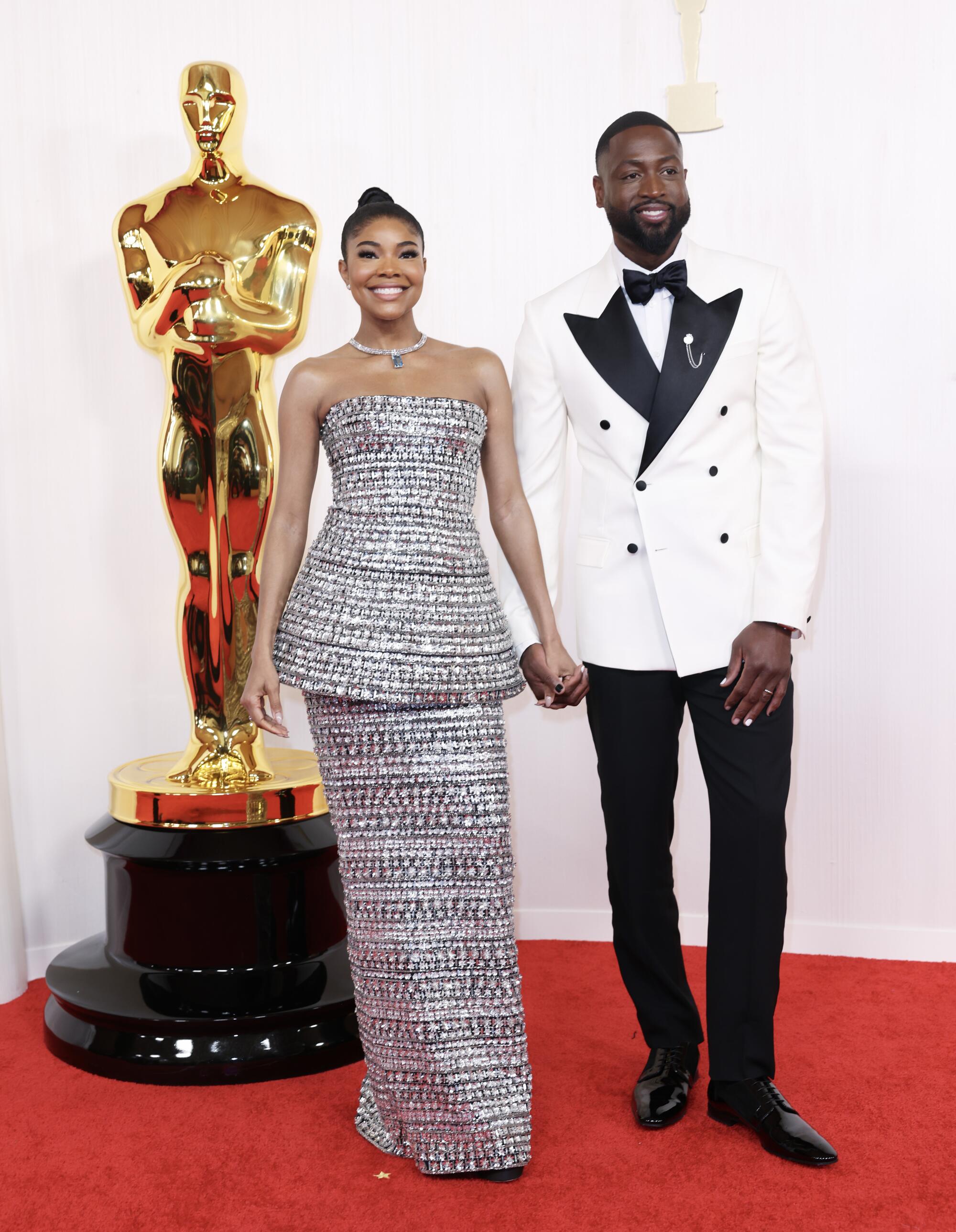Gabrielle Union, in a silver dress, and Dwyane Wade, in a white tux jacket and black pants, smile for cameras.