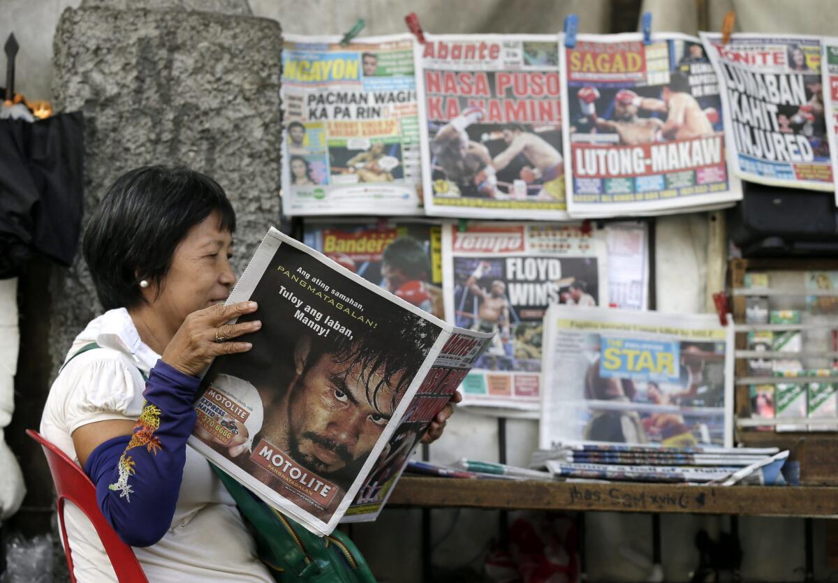 Una filipina lee un periódico que informa sobre el combate Mayweather vs Pacquiao en una calle de Manila, Filipinas.