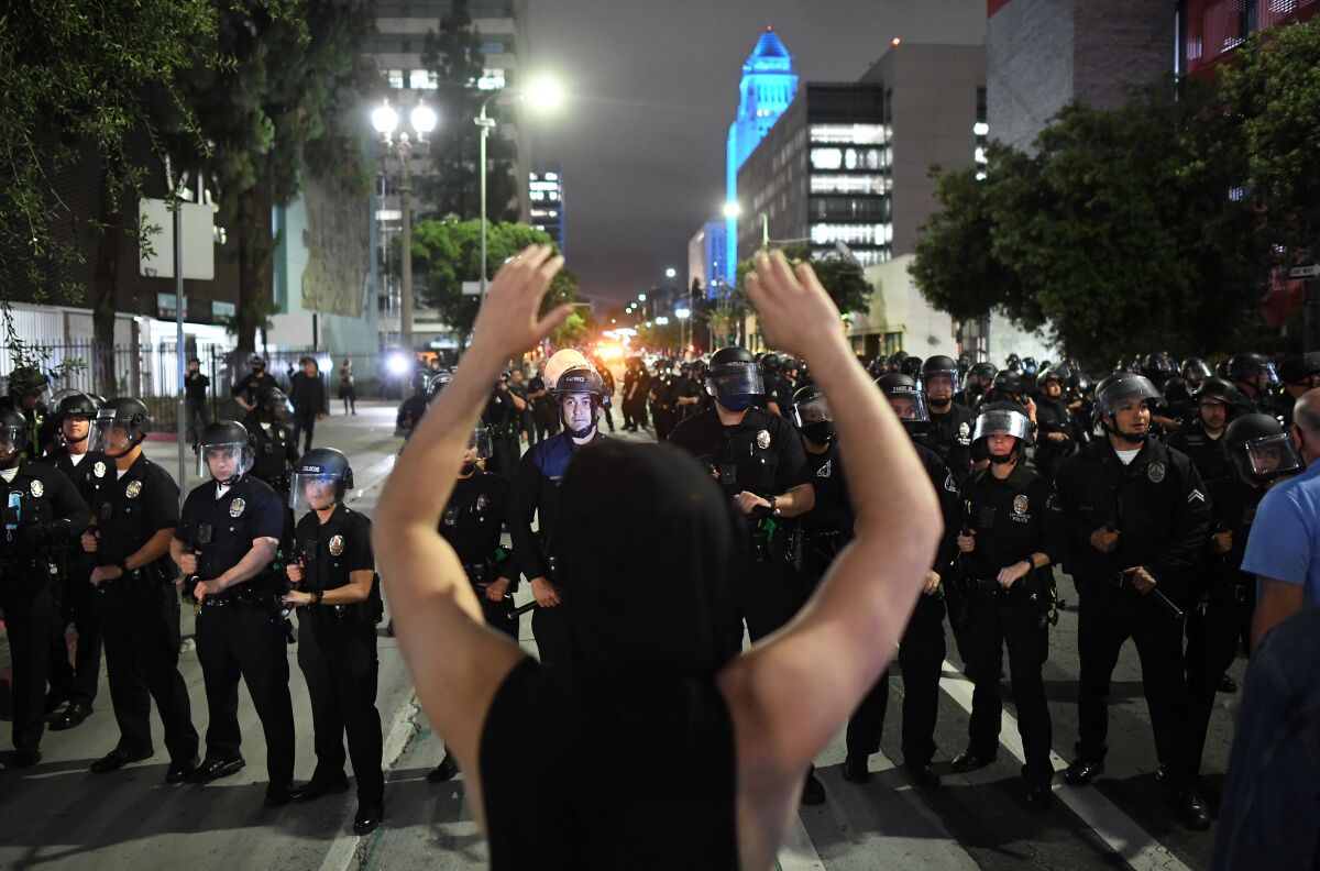 A protester raises his arms as LAPD officers approach on Spring St. in downtown Los Angeles on May 29