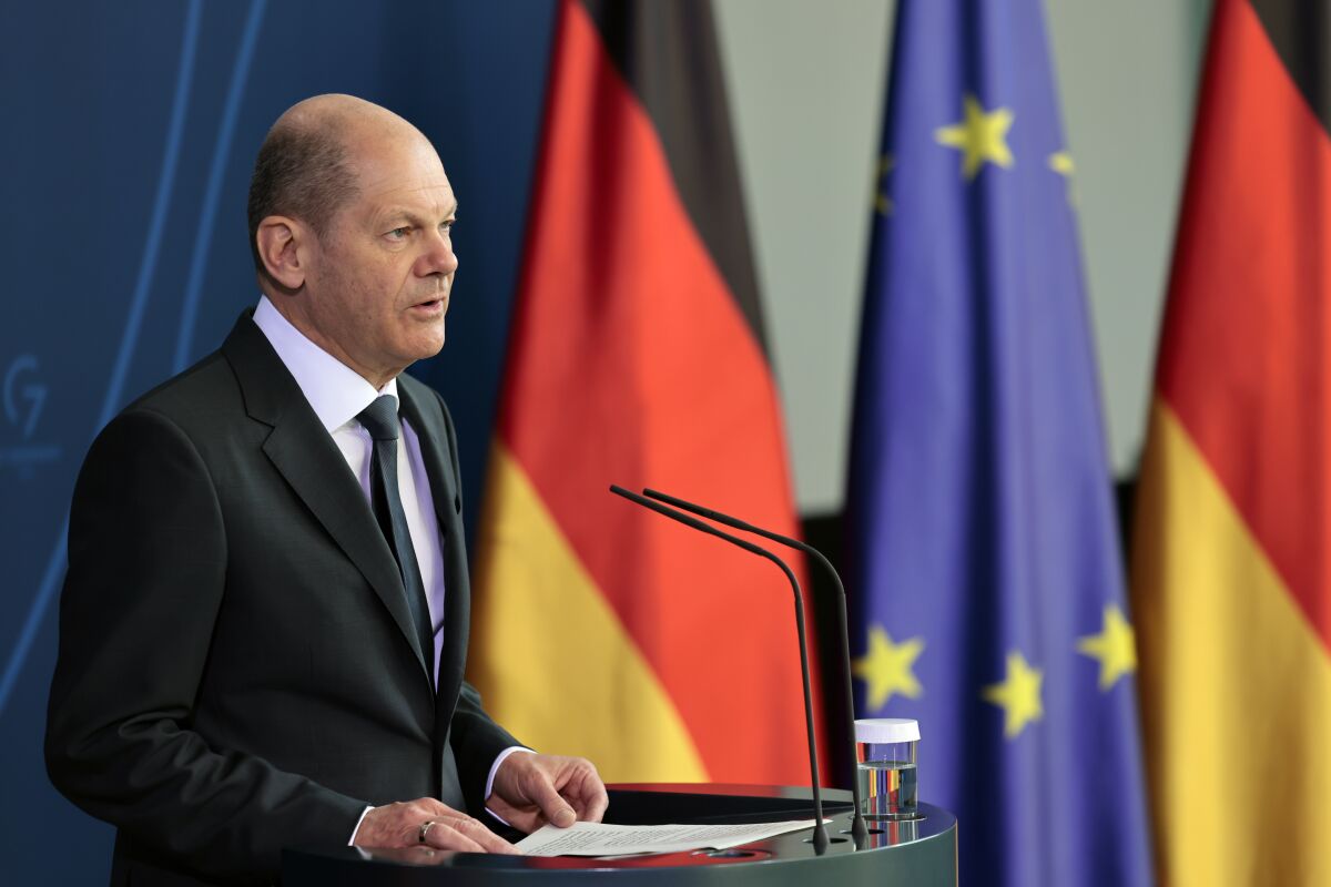 Man speaking at a lectern with German and EU flags in the background 