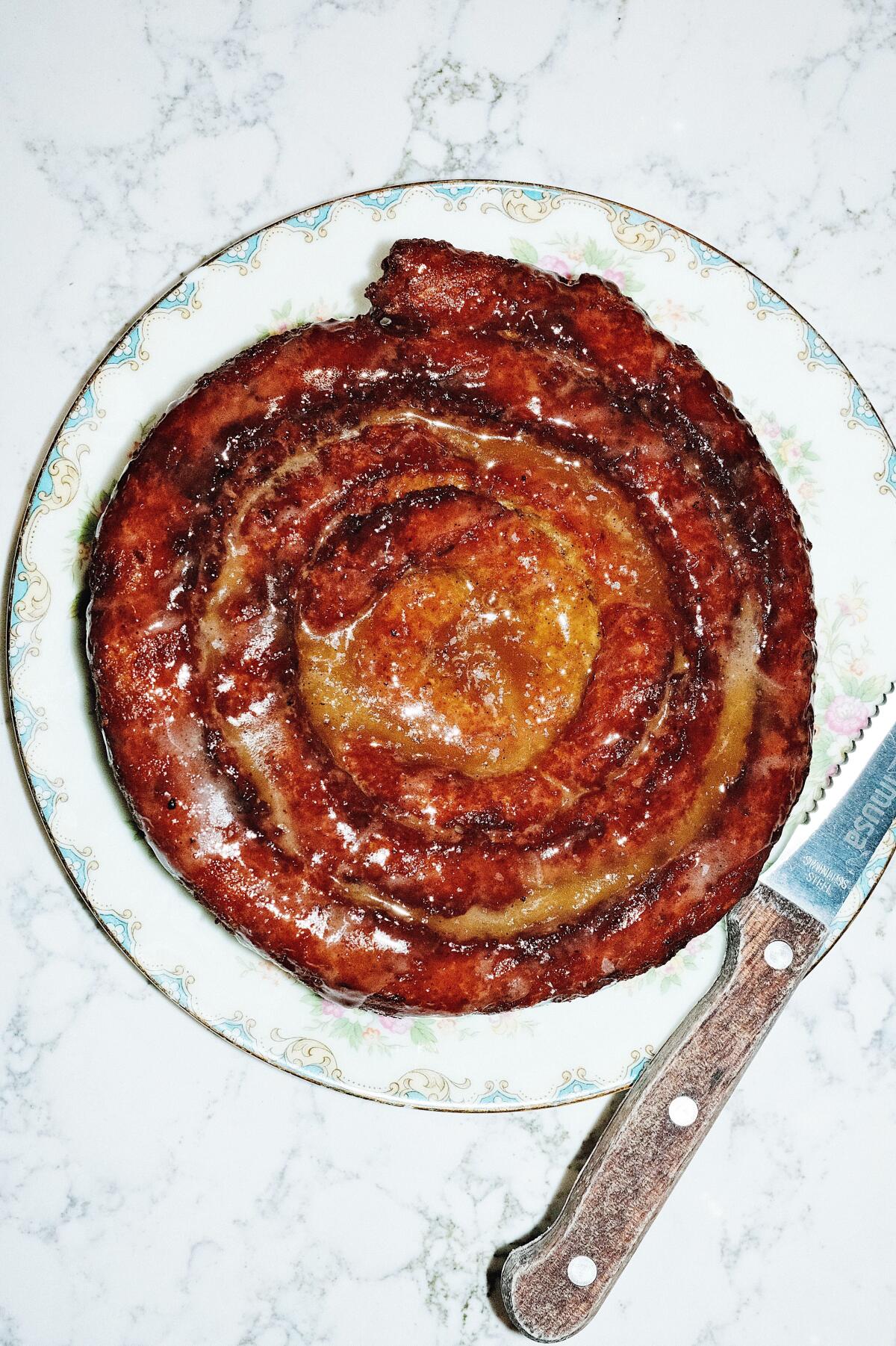 An overhead photo of a spiral pastry with a knife on the edge of the plate.