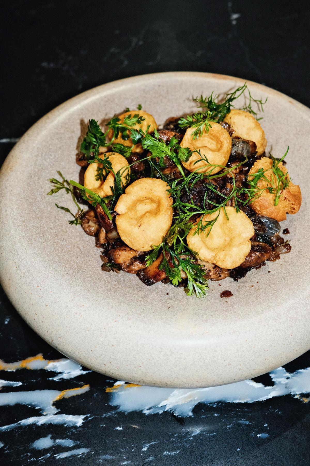 A gray bowl of chochoyotes atop a mix of mushroom and huitlacoche on a black table