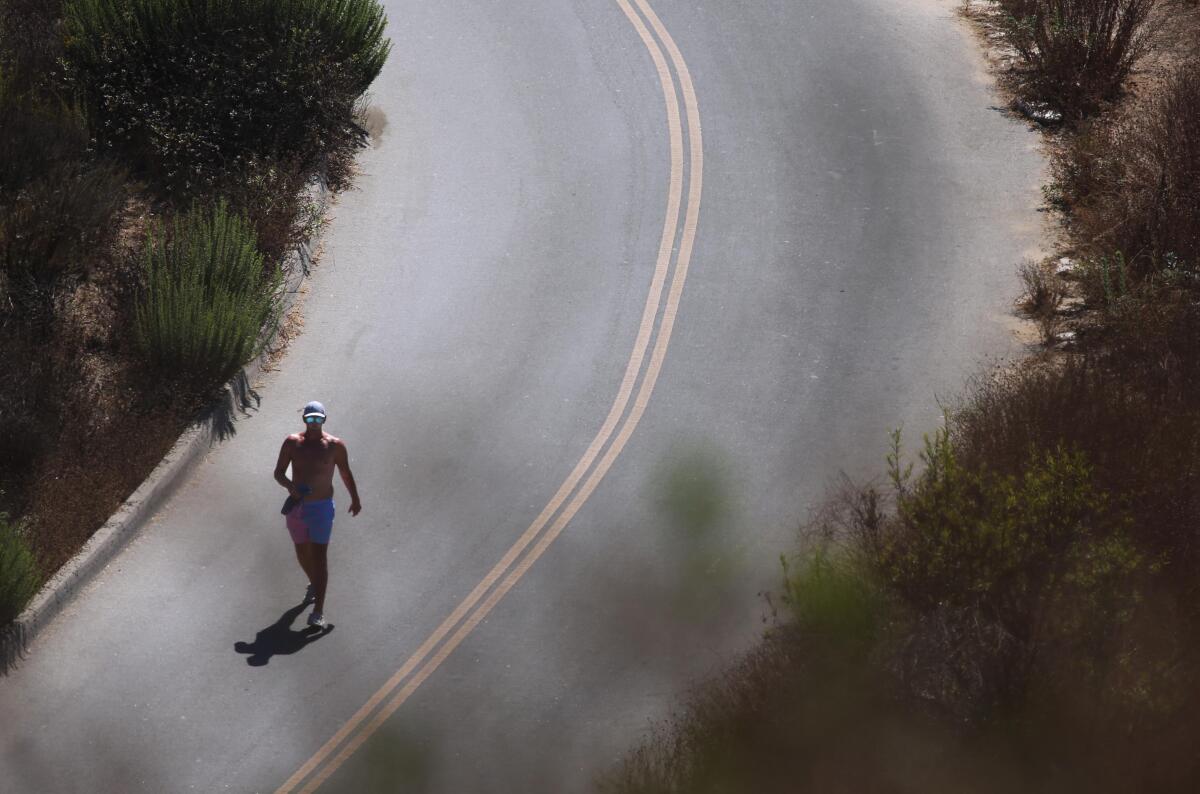 A shirtless man runs along a two-lane road with brush on either side.