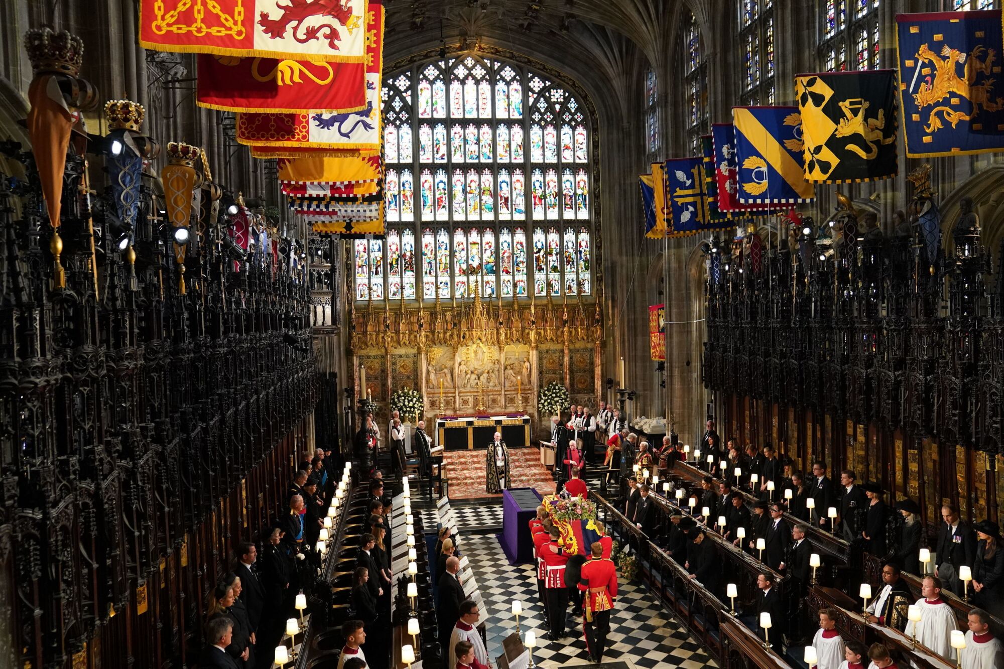 Uniformed pallbearers carry a casket through St. George's Chapel as attendees stand on pews on either side of the aisle.