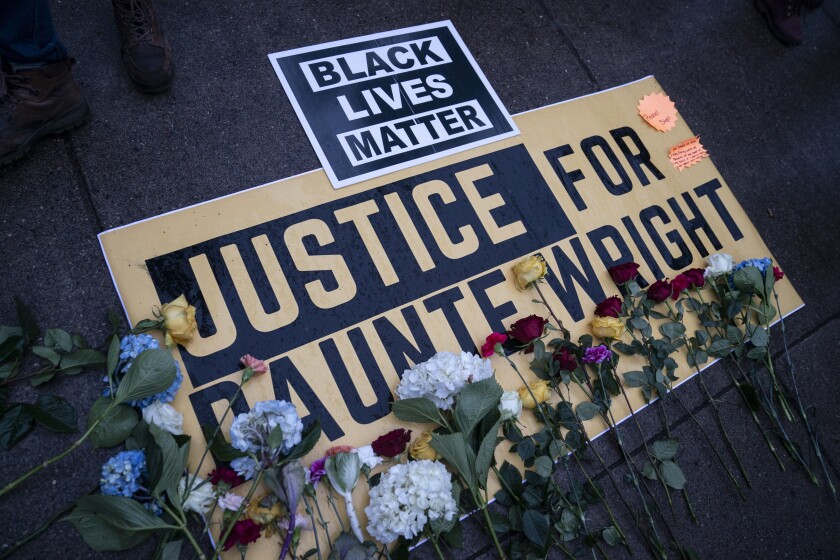 Flowers have been placed on a banner as demonstrators gather outside the Brooklyn Center (Minn.) Police Department on Tuesday, April 13, 2021, to protest Sunday's fatal shooting of Daunte Wright during a traffic stop. (AP Photo/John Minchillo)