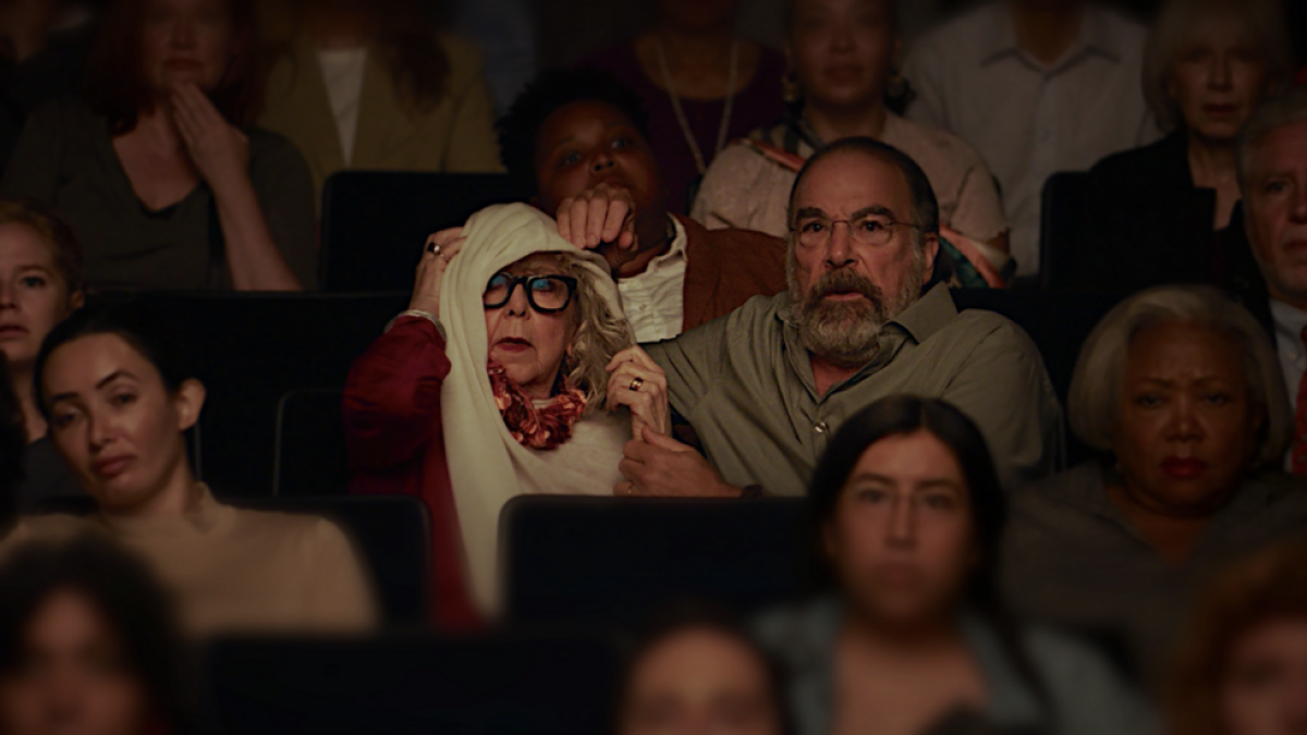 A woman and a man sitting in theater seats with surprised expressions.