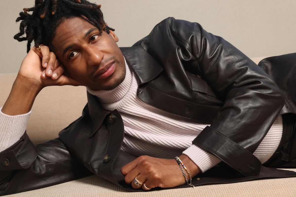 Singer-songwriter Jon Batiste lies on his side, head propped on his raised arm for a portrait. 