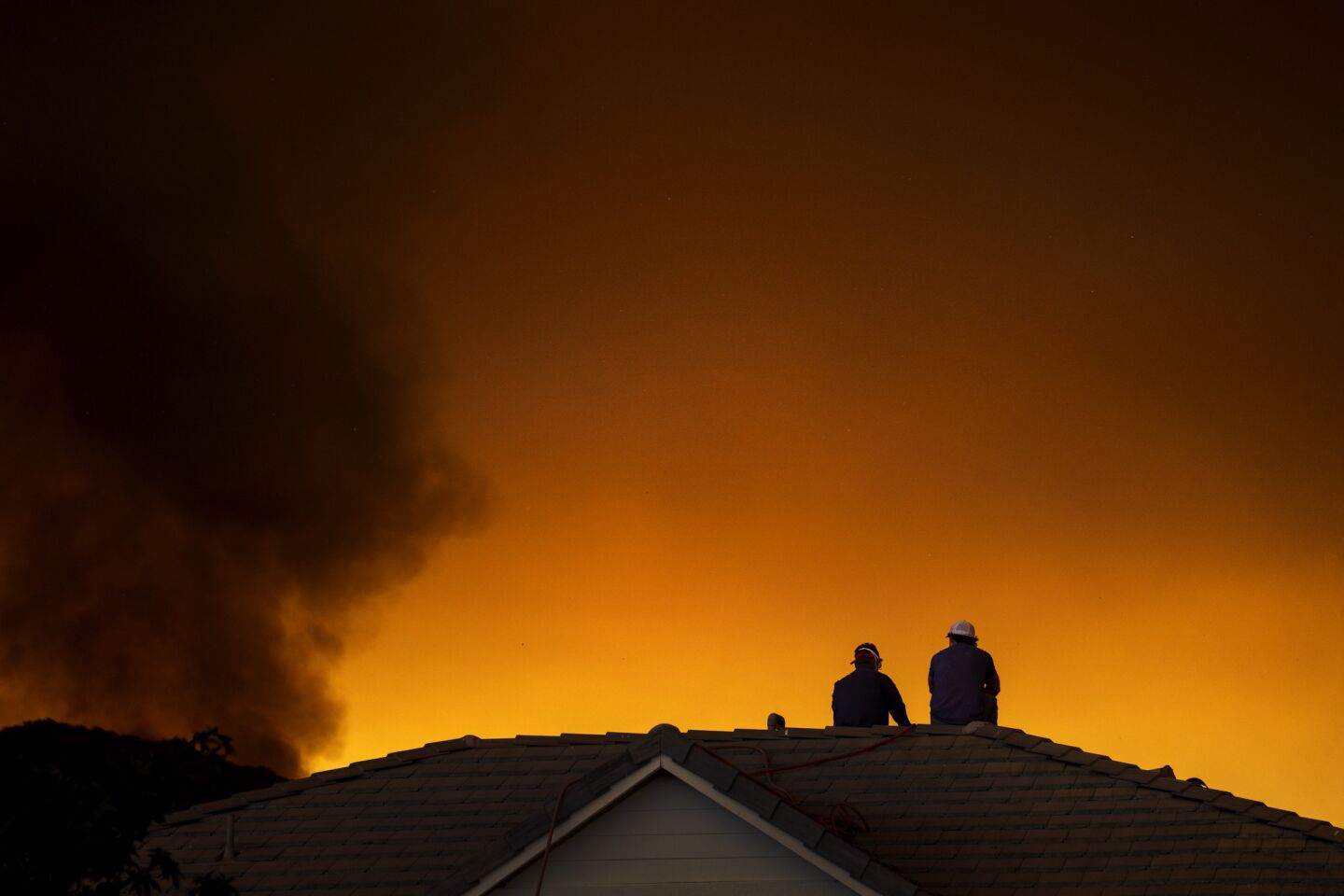 Two men monitor the Holy fire from a rooftop as it approaches the McVicker Canyon neighborhood in Lake Elsinore.