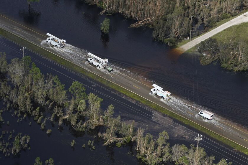 Power company crew trucks drive on a flooded street on their way to help communities impacted by Hurricane Ian, Thursday, Sept. 29, 2022, in Fort Myers, Fla. (AP Photo/Marta Lavandier)