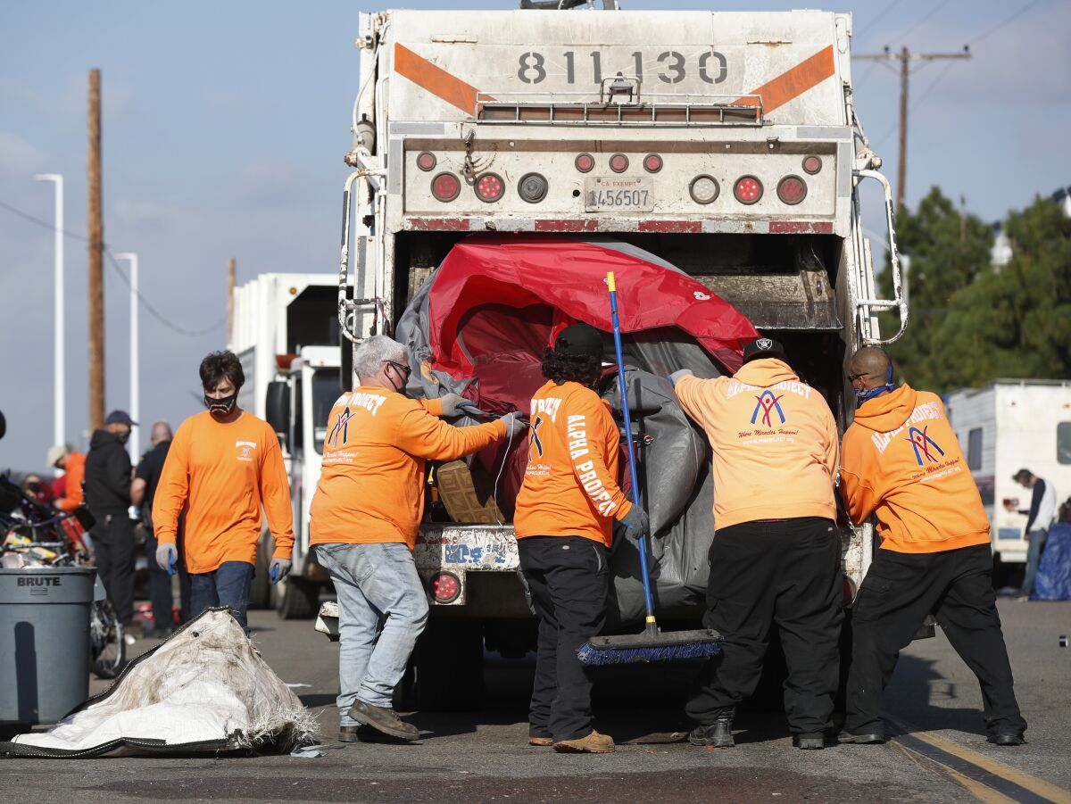 Workers for the Alpha Project and the city of San Diego throw a tent into a trash truck during a cleanup Tuesday morning.