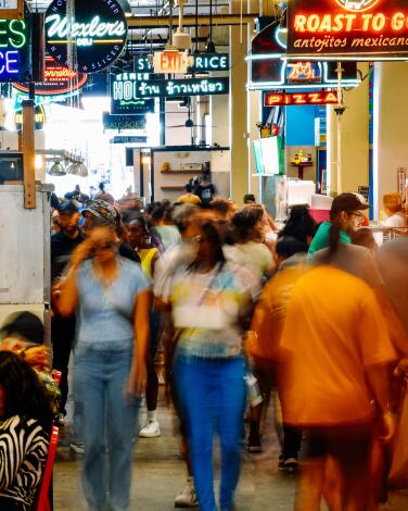 Long-exposure photo of people walking among food and fruit stalls at Grand Central Market