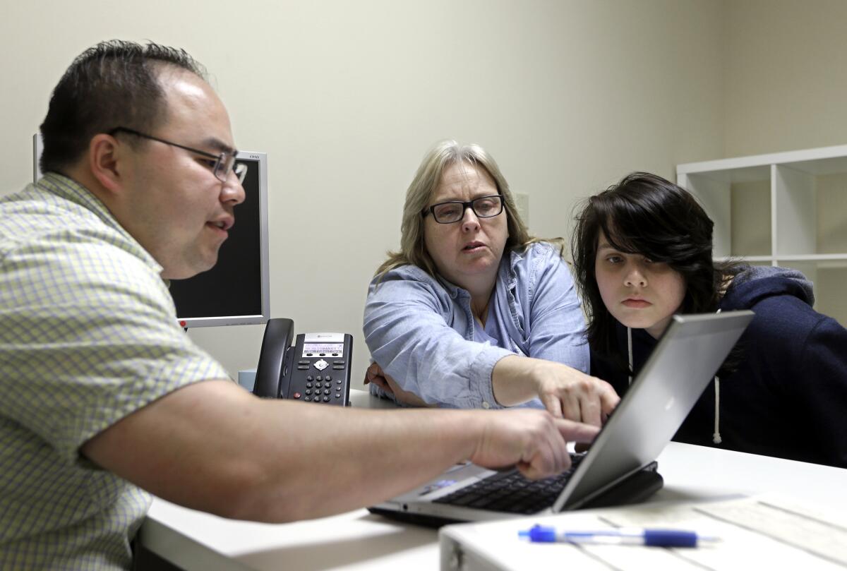 Three people looking at a laptop screen in an office