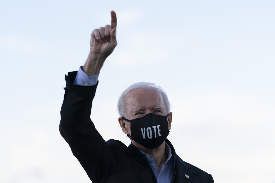 President-elect Joe Biden, in a mask that says "Vote," holds up his right arm.