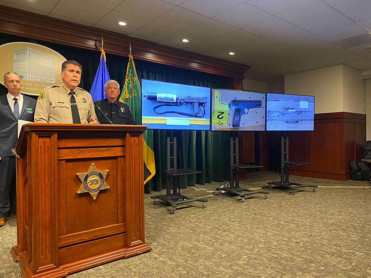Sheriff speaks in front of three screens showing images of an assault pistol with an attachment, a handgun and a rifle