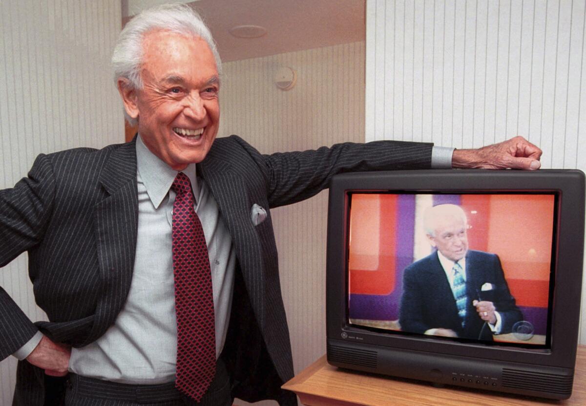 Bob Barker leans on his hotel room television showing his image.