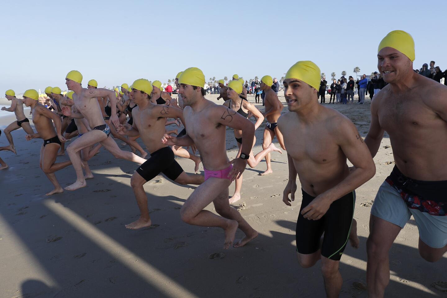Participants race to the ocean on the north side of the pier as they compete in the 1,000 yard open water swim event during Huntington Beach's lifeguard tryouts on Saturday.