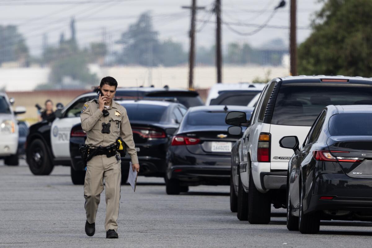 A law enforcement officer walks down a street while on a phone.