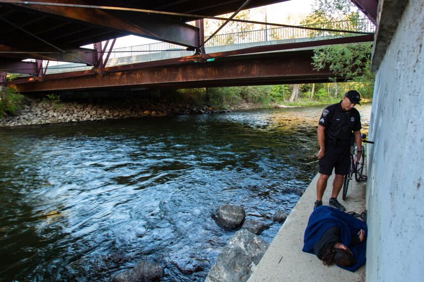 Sgt. Craig Nixon of the Boise Police Department's Micro District Bike Patrol talks with a homeless man by the Boise River on a footing of the Eighth Street pedestrian bridge in Boise, Idaho on August 28, 2019.