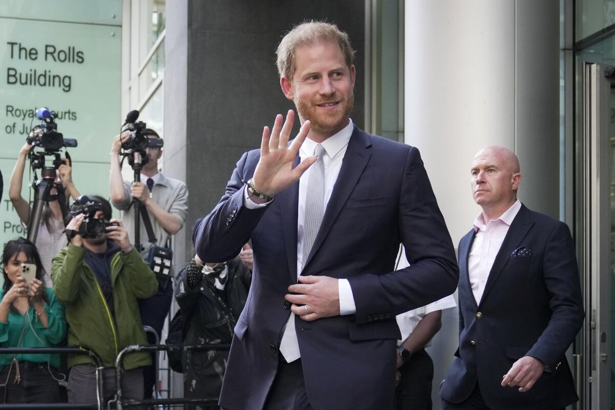 Prince Harry smiles and waves in suit as photographers take his picture on his way out of a British courthouse