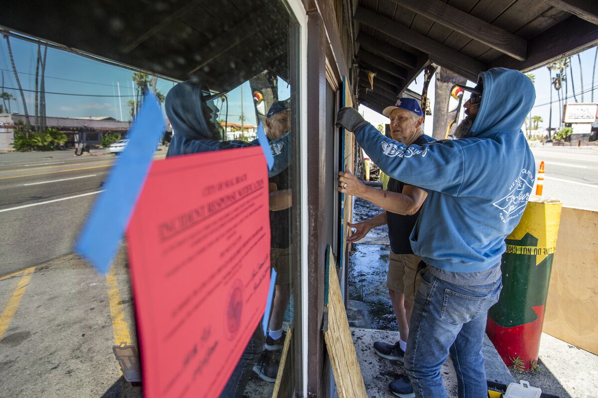 Todd Maris, right, owner of Taco Surf in Surfside, and Richard McCarty board up windows after a fire broke out Friday. 