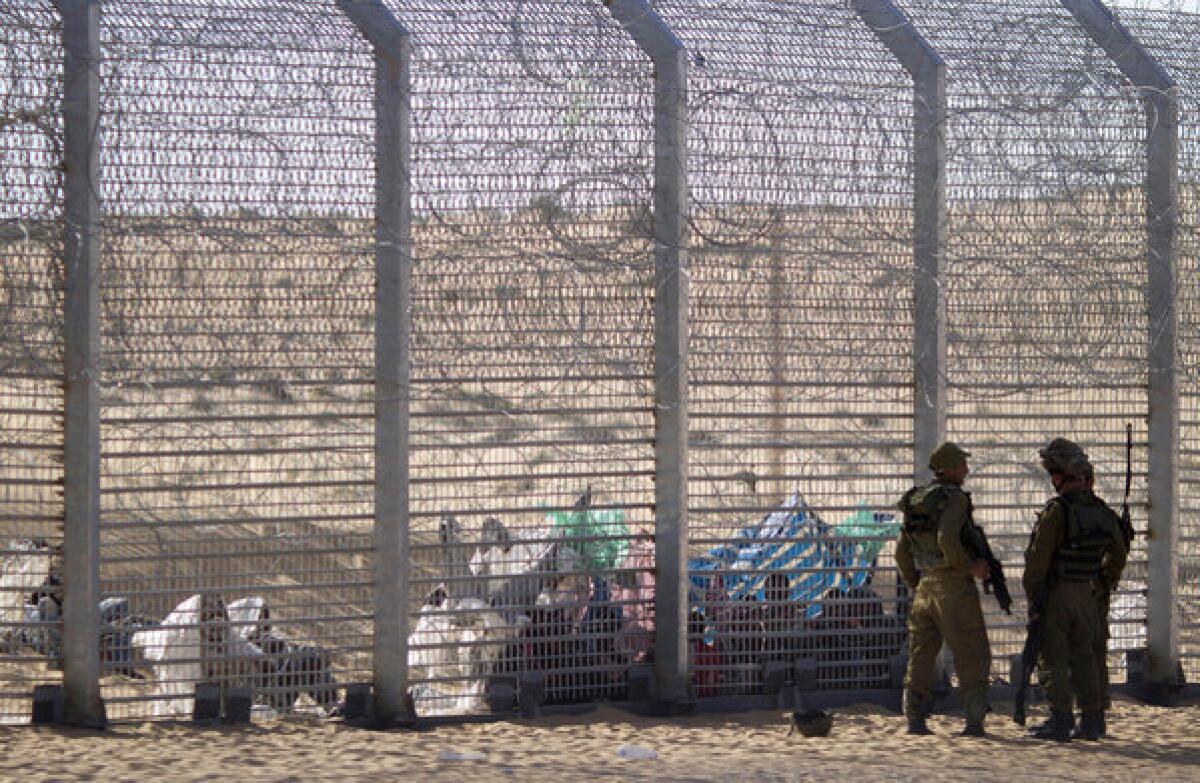African refugees sit on the ground behind a border fence after they attempted to cross illegally from Egypt into Israel, as Israeli soldiers stand guard near the border with Egypt, in southern Israel.