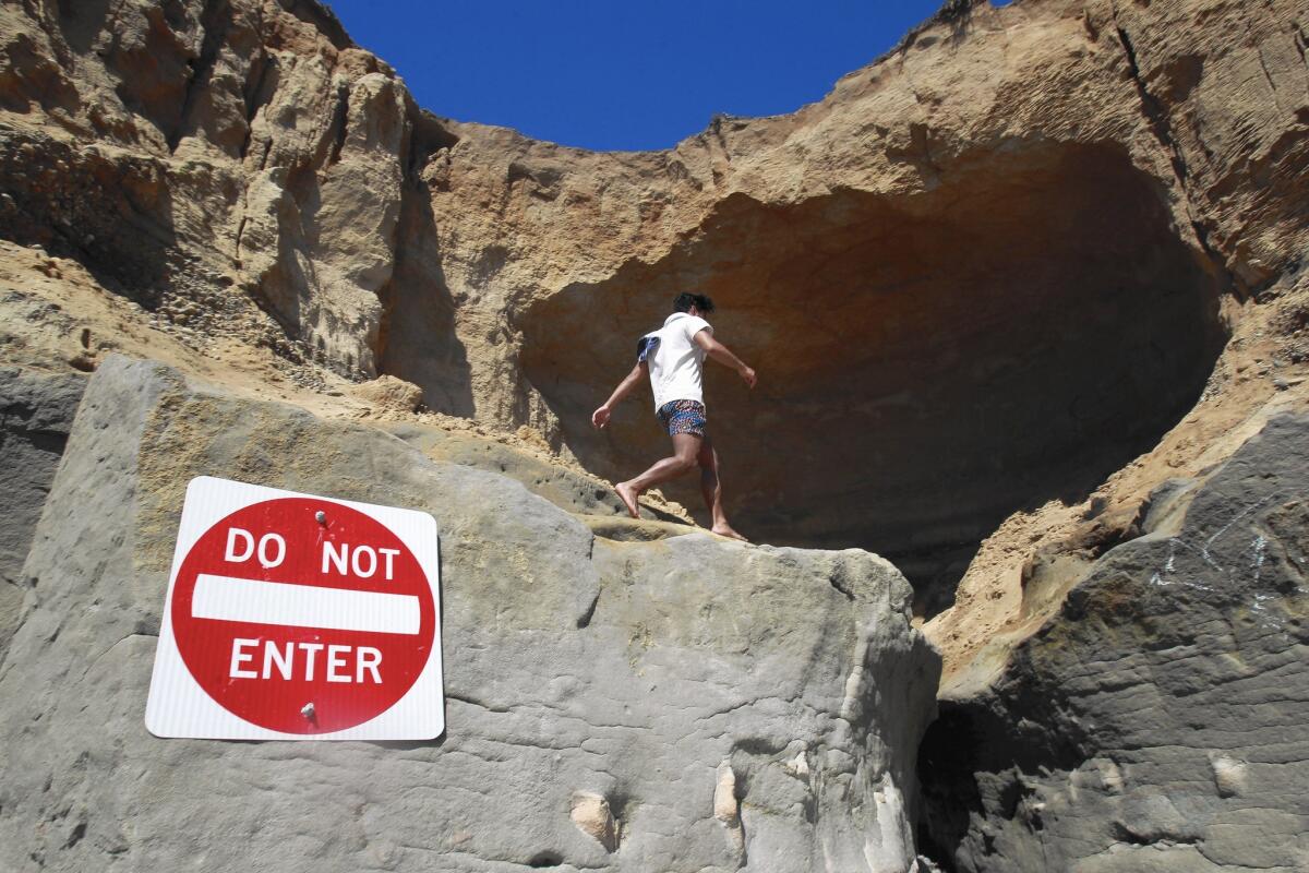 Steven Balubar walks near a sea cave that has opened up beneath a Carlsbad bluff. The cave — in the city’s Terramar area — has prompted authorities to post warning signs and cordon off the top of the cliff.