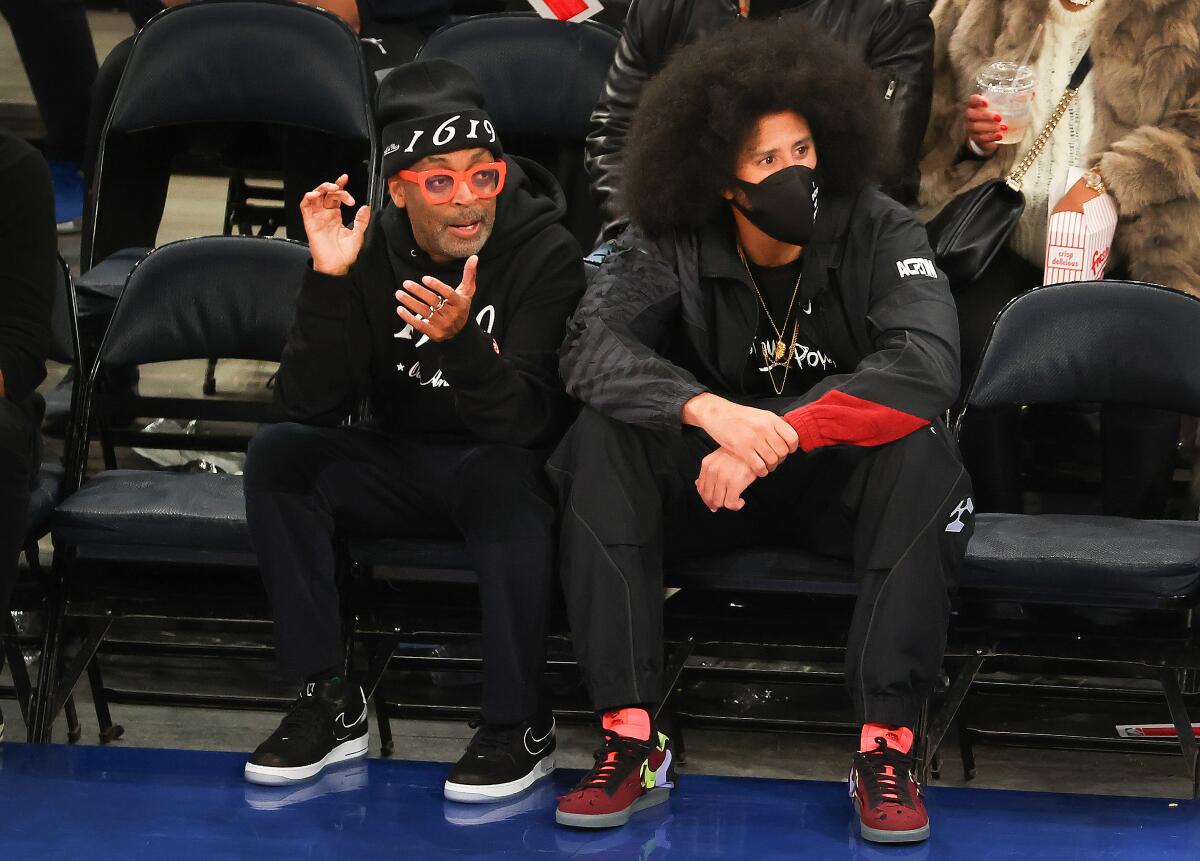 Two men sit courtside at a basketball game.