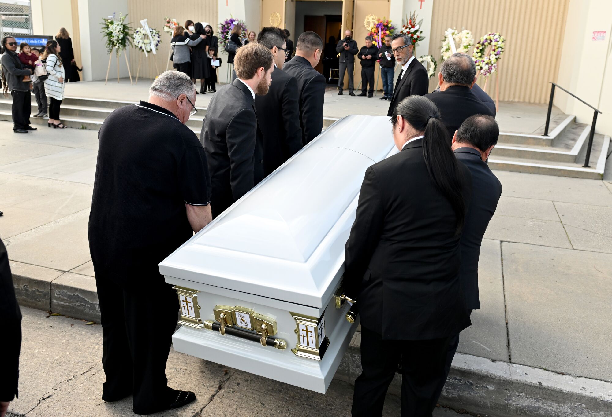 Men carry a casket from the curb onto the sidewalk in front of a church entrance