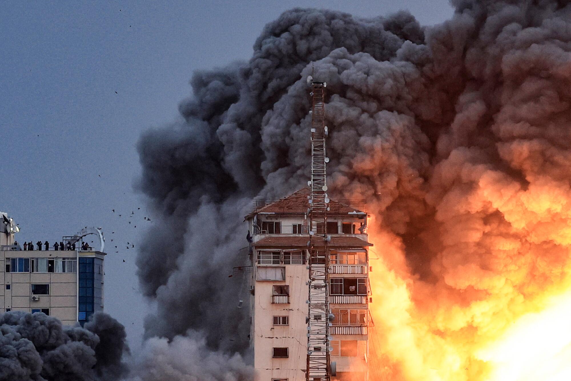 People standing on a rooftop watch as a ball of fire and smoke rises above a building in Gaza City.