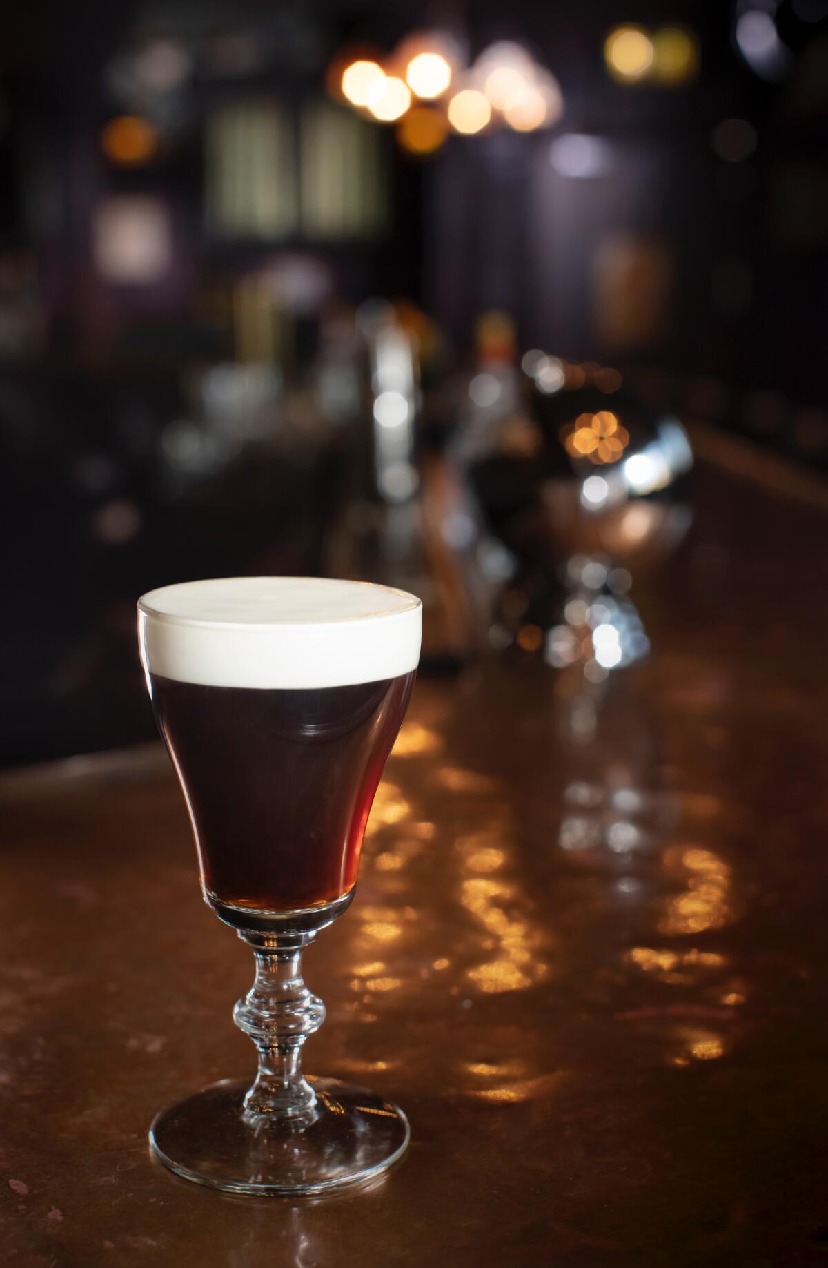 Irish coffee in a tulip glass with a white foamy head, sitting on a wooden bar.