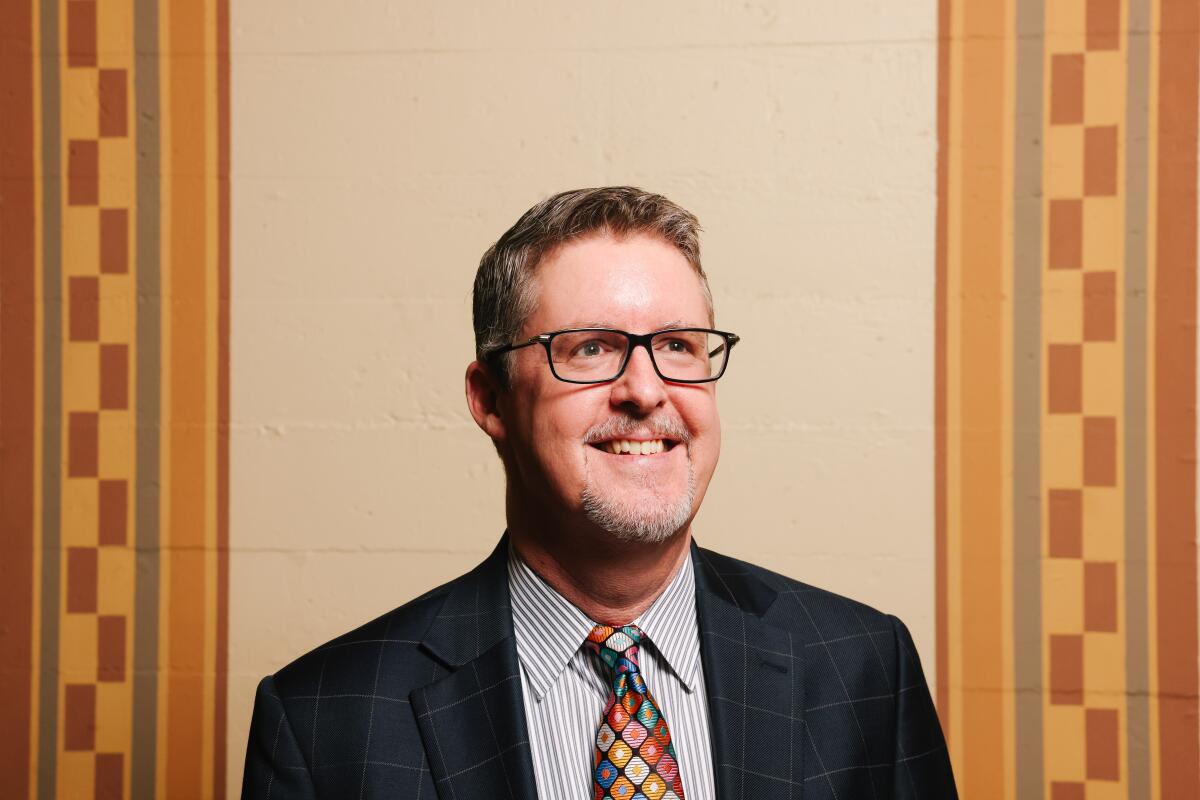 A smiling man in glasses and a suit between two geometric wall stripes