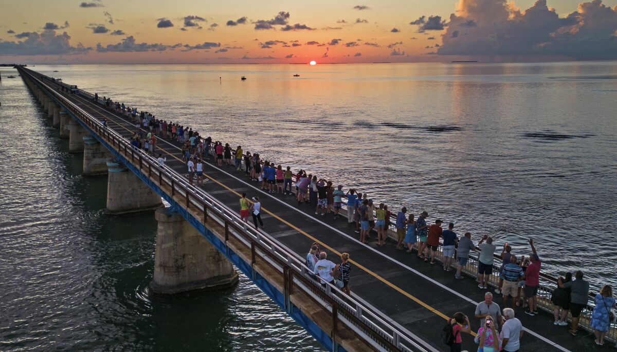 In this aerial photo provided by the Florida Keys News Bureau, attendees watch and toast the sunset at a Florida Keys bicentennial celebration, Friday, May 19, 2023, on the restored Old Seven Mile Bridge in Marathon, Fla. The sunset gathering was among a series of Keys events being staged to mark the 200th anniversary, on July 3, of the Florida Territorial Legislature's 1823 founding of Monroe County, containing the entire island chain. The old bridge was originally part of Henry Flagler's Florida Keys Over-Sea Railroad completed in 1912, and is now closed to vehicles but open to pedestrians and bicycles. (Andy Newman/Florida Keys News Bureau via AP)