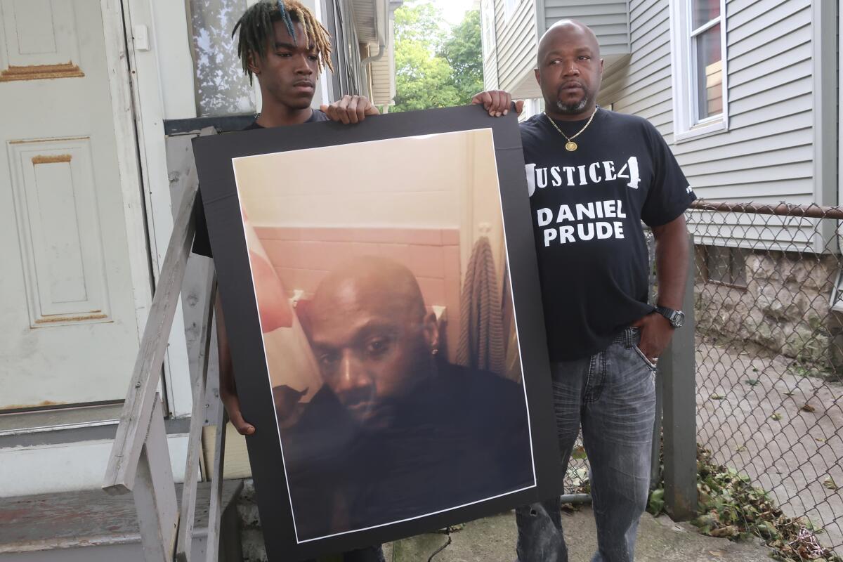 Two men, one in a "Justice for Daniel Prude" shirt hold up a poster of Prude.