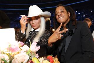 Beyonce tips her white cowboy hat and Jay Z makes a peace sign at a Grammy Awards table