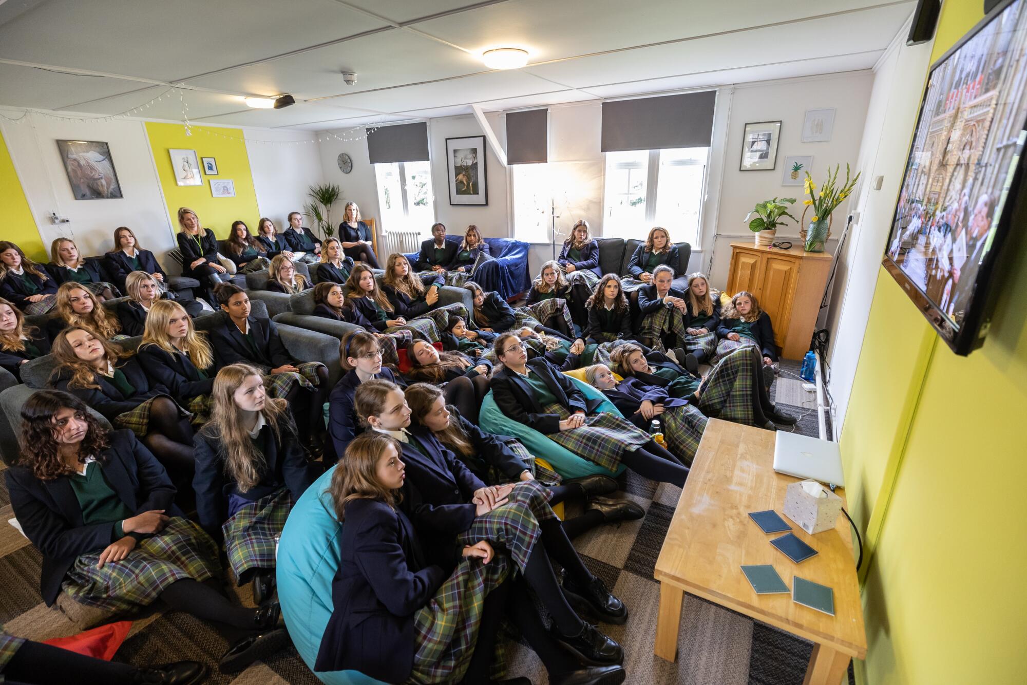 A crowd of students fills a room to watch a TV.