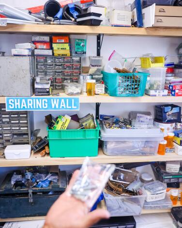 A hand holds up a plastic bag of nails in front of a tool shelf at Makers Hub.