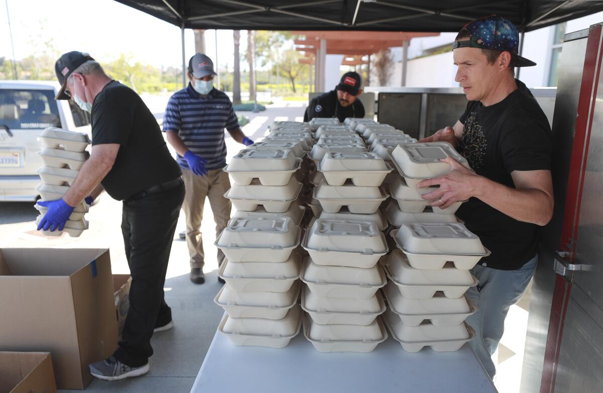 O'side Kitchen Collaborative Director of Operations Mike Perez, right, and volunteers prepare to load vehicles with prepared dinners for senior communities at the O'side Kitchen Collaborative on Tuesday, March 24, 2020 in Oceanside, California.