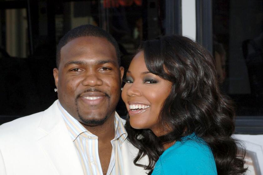 A man with short black hair in a white suit, left, and a woman with long black hair in a blue shirt both smiling and posing