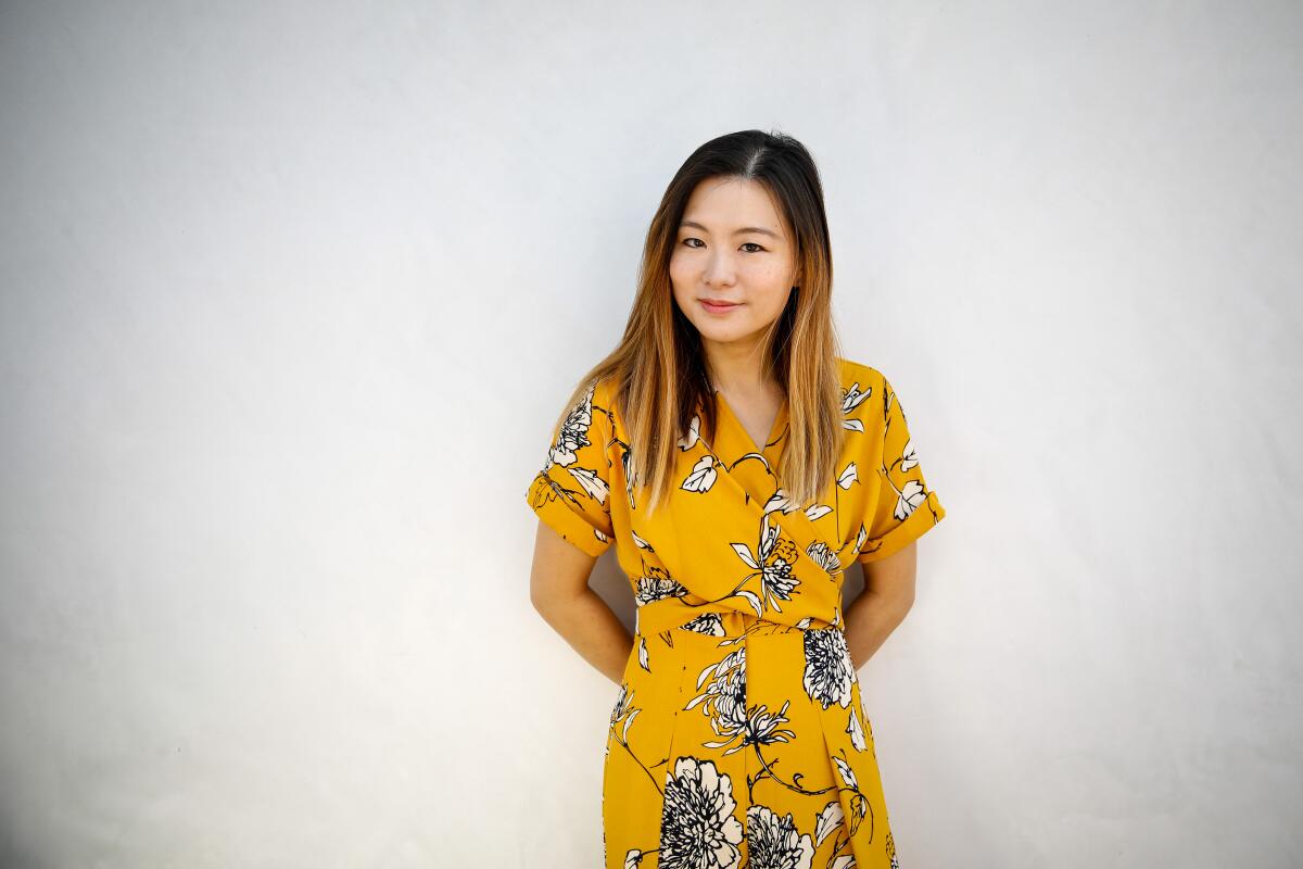 Jenny Wong stands against a white wall in a bright floral yellow pant and blouse suit